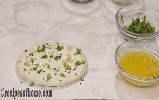 stretch naan dough to oval shape and add coriander leaves,garlic,kalonji seeds and butter